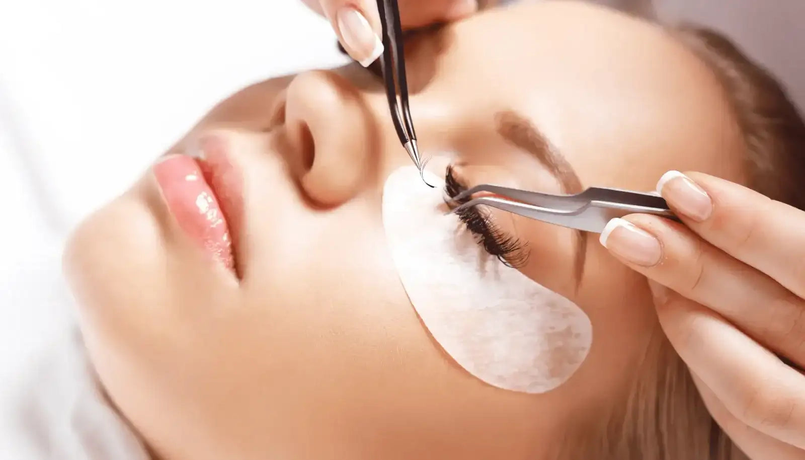 A pair of black, slender tweezers delicately holds a single dark eyelash for application.