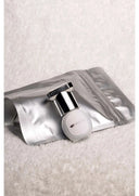 A sleek white cylindrical pro master adhesive bottle with chrome cap on silver foil pouch for professional lash artists